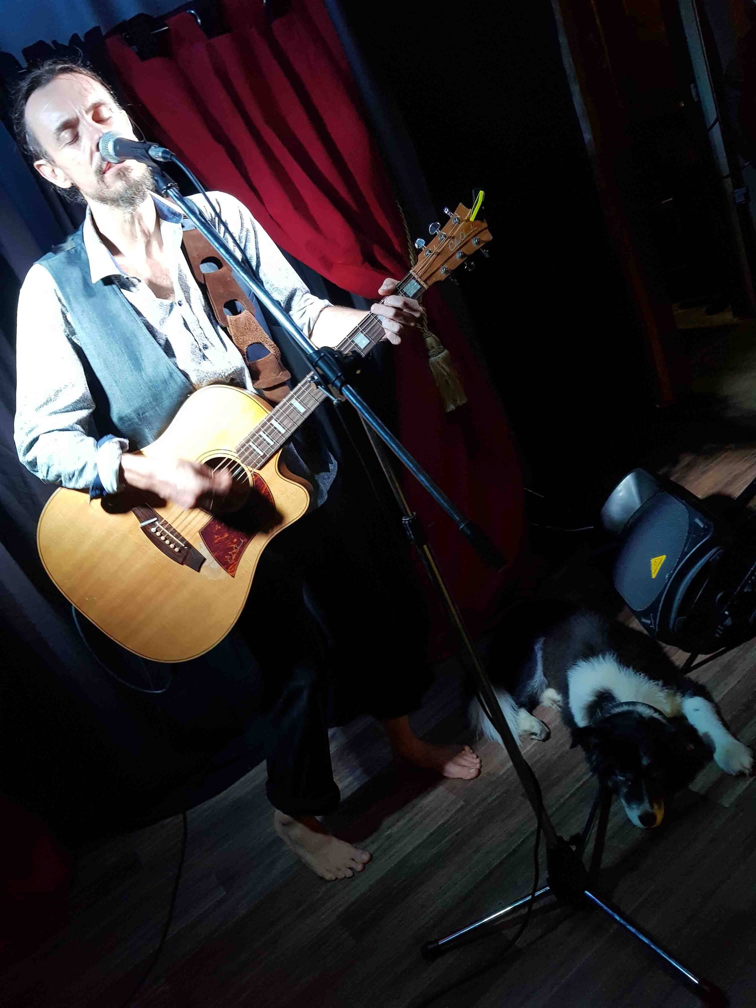 Kieran Wicks Performing Live singing and playing guitar on Stage in Mackay, Border COllie dog asleep on stage Red Stage Curtains